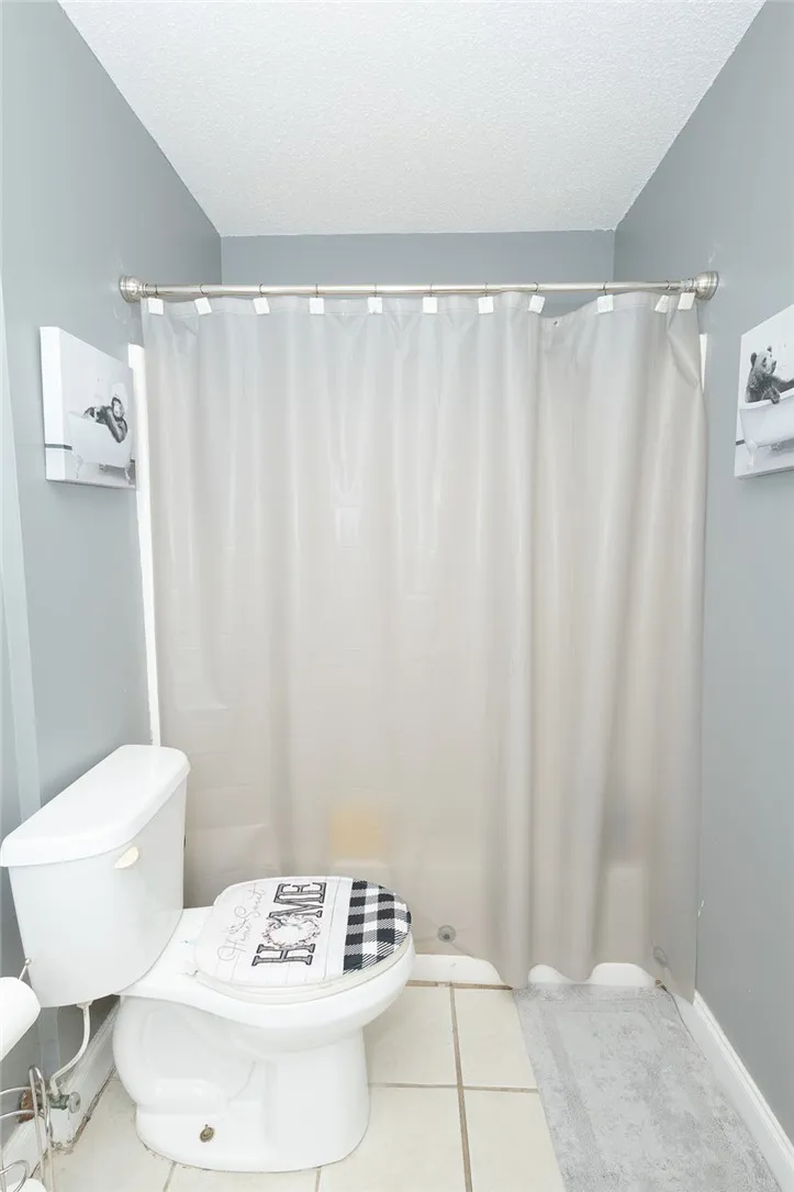 Functional bathroom featuring a shower with a privacy curtain and durable tile flooring.