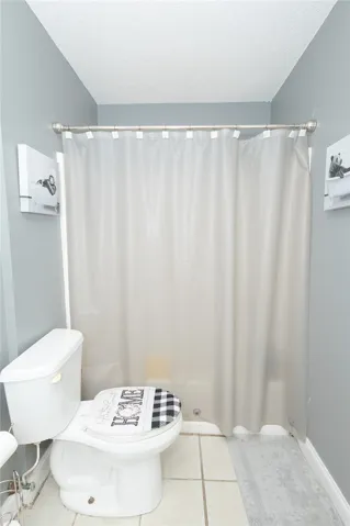 Functional bathroom featuring a shower with a privacy curtain and durable tile flooring.