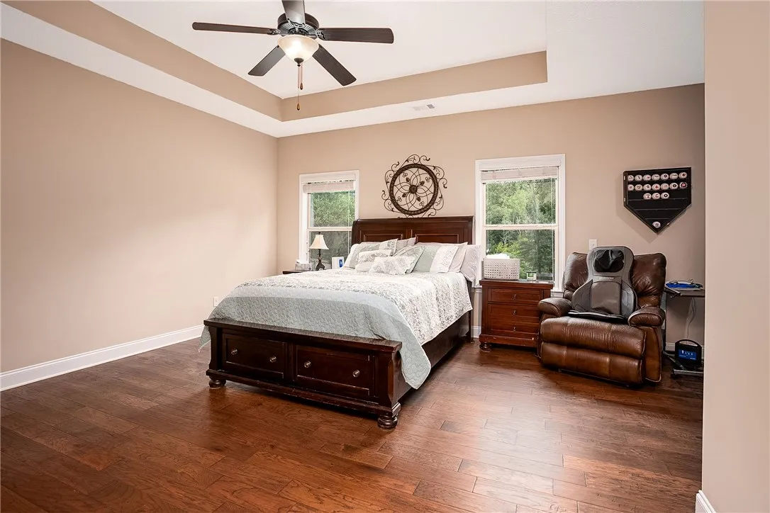 Rich hardwood floors and a tray ceiling with a ceiling fan define this spacious primary bedroom.
