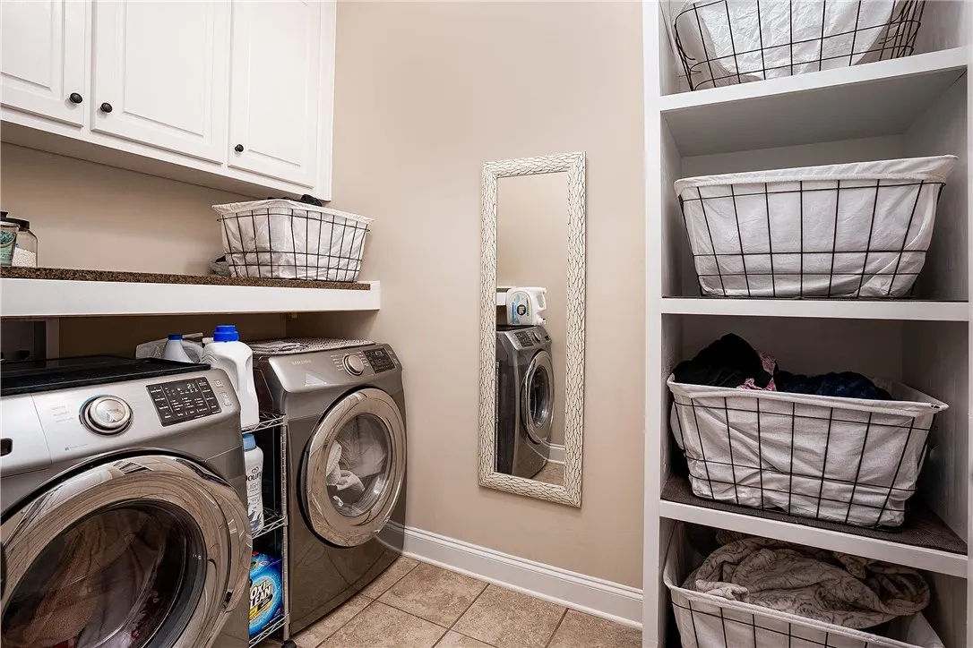 Functional laundry room featuring tile flooring, convenient shelving, and pristine white cabinetry.