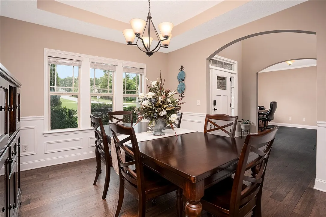 Hardwood floors and a sophisticated chandelier create an inviting atmosphere for dining, with a view of the manicured outdoor landscaping.