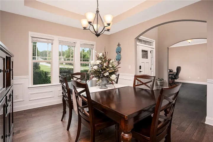 Hardwood floors and a sophisticated chandelier create an inviting atmosphere for dining, with a view of the manicured outdoor landscaping.