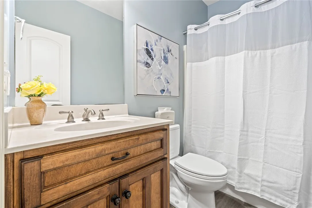 A warm wooden vanity with a sleek white countertop complements the soft blue walls in this tidy bathroom.
