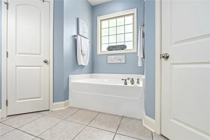 A deep soaking tub awaits in this serene bathroom, complete with elegant tile flooring and a multi-paned window.