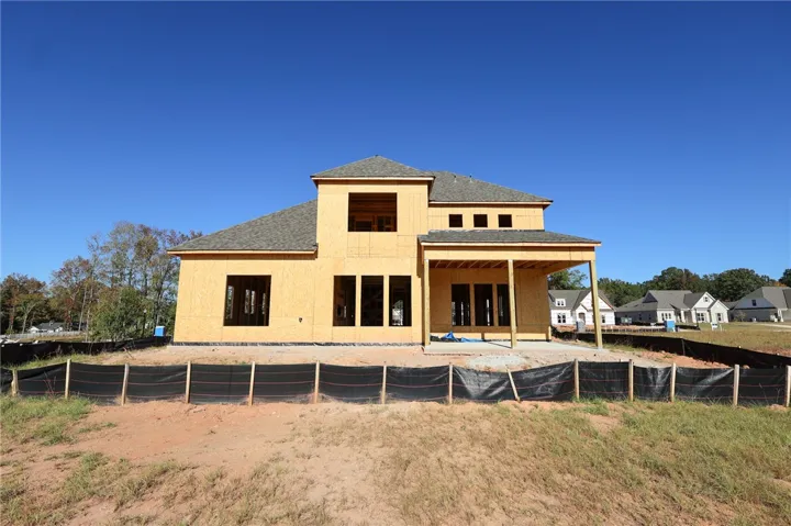 An unfinished residential structure showcases a soaring roofline and a covered patio foundation.