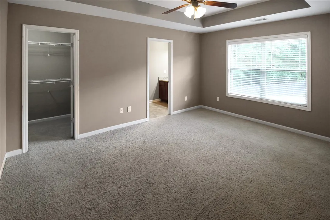 A spacious primary bedroom featuring a tray ceiling, ceiling fan, and plush carpeting.
