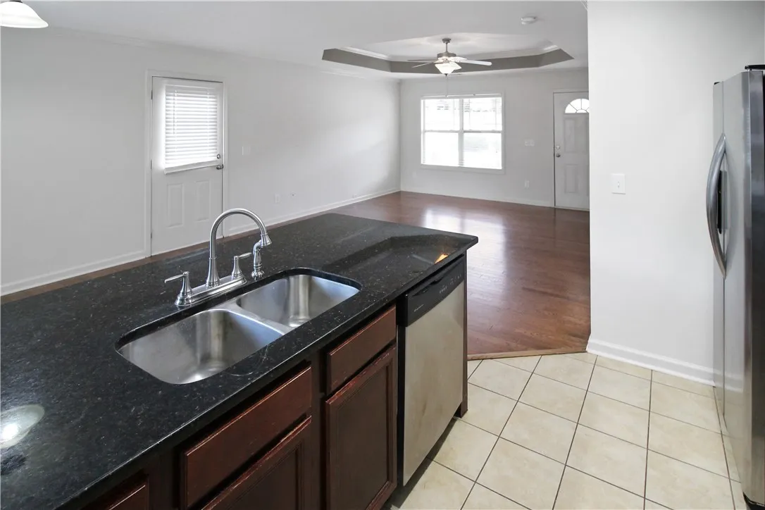 A well-lit kitchen with dark granite countertops overlooks a warm hardwood living area.