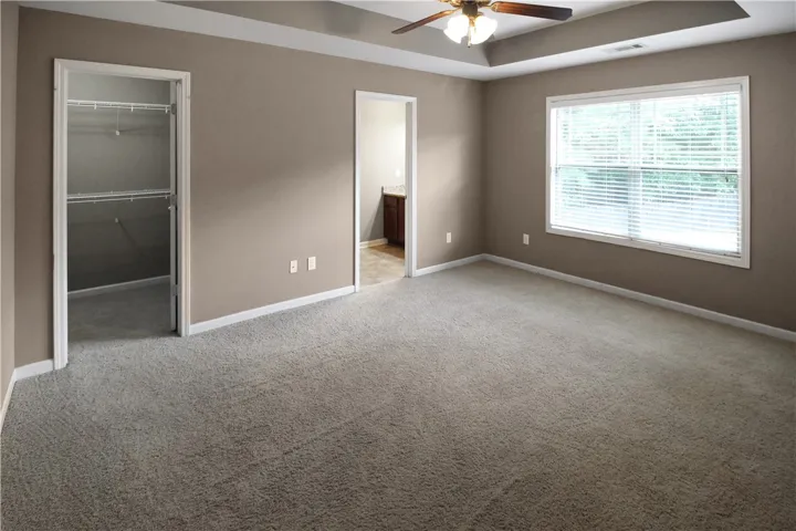 A spacious primary bedroom featuring a tray ceiling, ceiling fan, and plush carpeting.