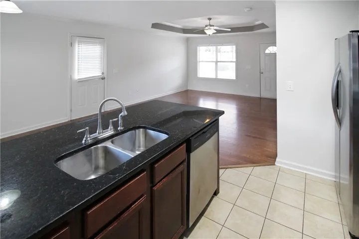 A well-lit kitchen with dark granite countertops overlooks a warm hardwood living area.
