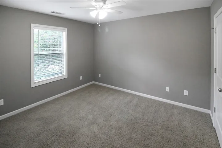 A well-lit bedroom with soft carpet flooring and a simple ceiling fan, offering a tranquil personal retreat.