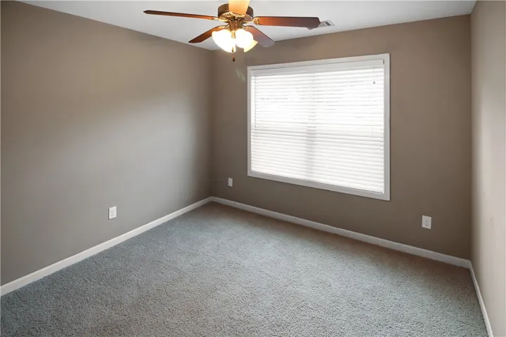 A well-lit bedroom offering plush carpet and a convenient ceiling fan for year-round comfort.