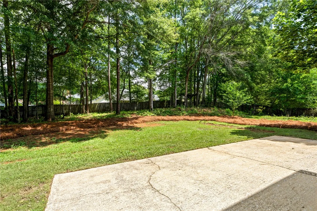 A well-maintained yard offers a concrete patio and a natural tree line for ultimate privacy.