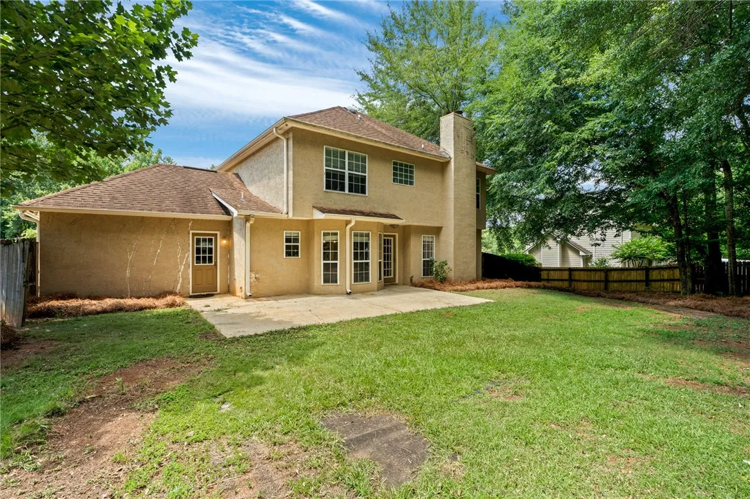 A spacious backyard with mature trees, a private fence, and a concrete patio.