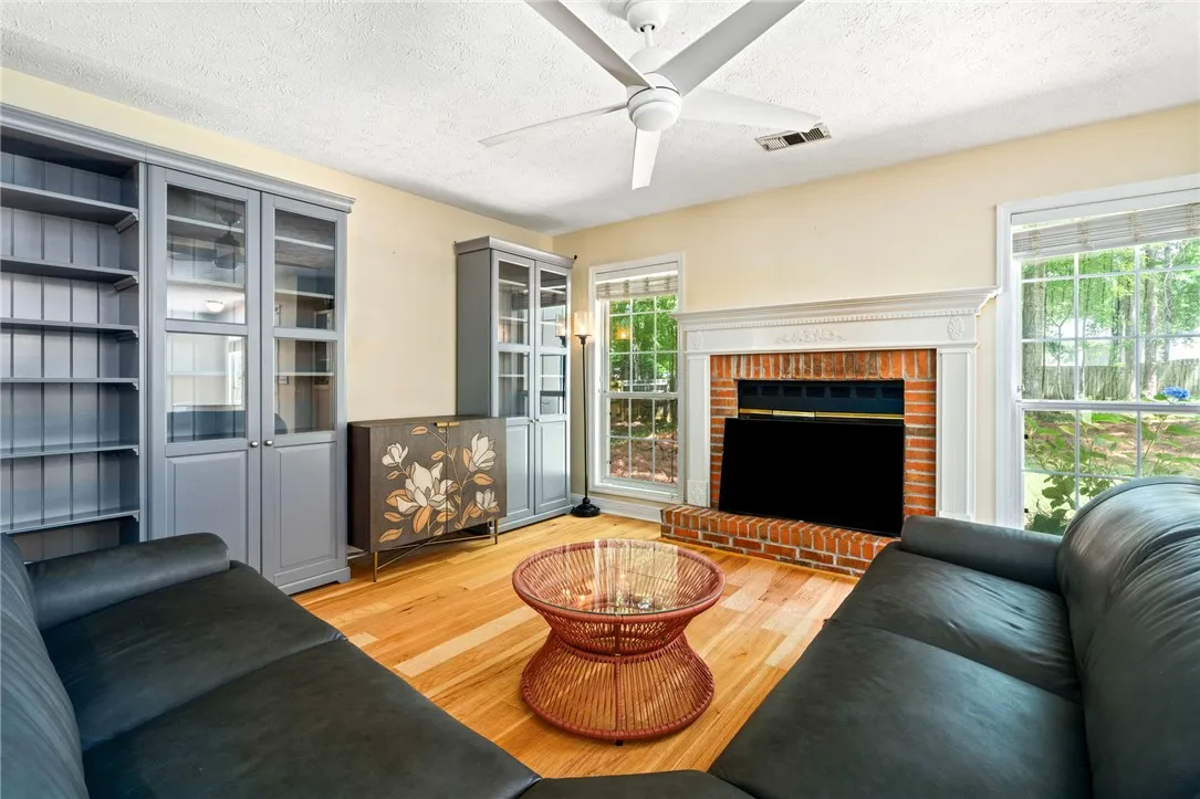 Bright hardwood floors complement the cozy brick fireplace and built-in shelving, creating a welcoming living space.