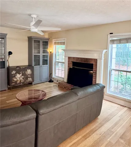 A well-lit living space features a cozy brick fireplace and gleaming hardwood floors.