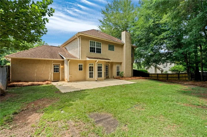 A spacious backyard with mature trees, a private fence, and a concrete patio.