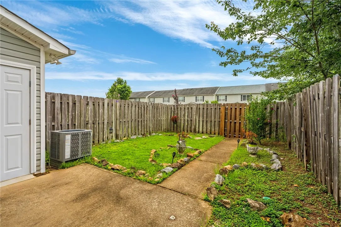 A quaint backyard space, fully fenced, with a concrete patio and walkway leading to a private gate.