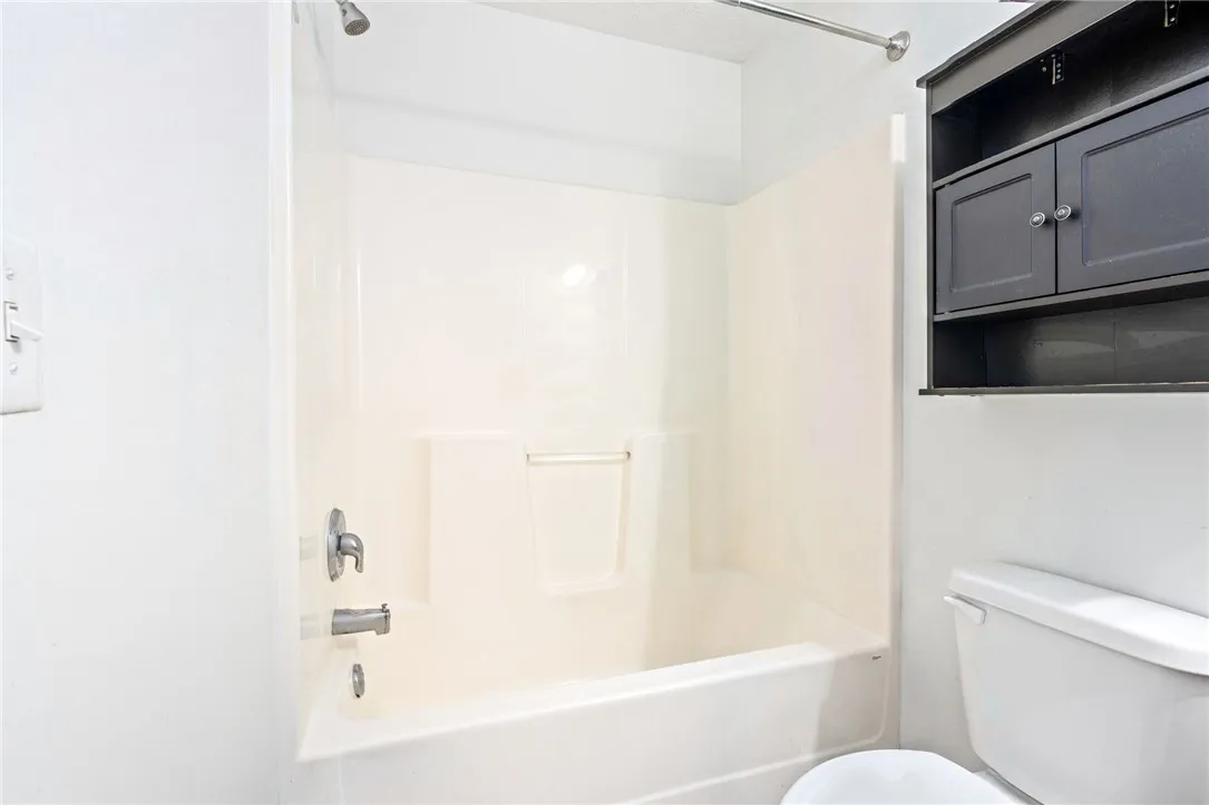 A pristine bathroom featuring a tub and shower combination, complemented by practical storage above the commode.