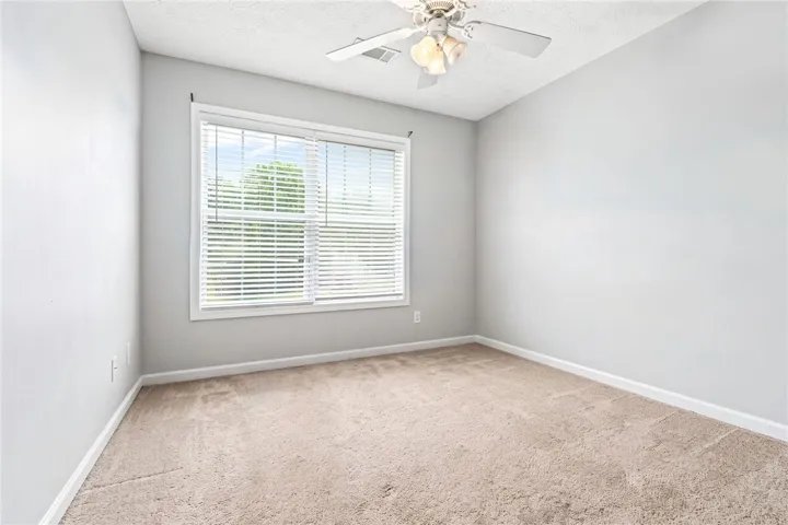 A well-lit bedroom features plush carpeting and a convenient ceiling fan.
