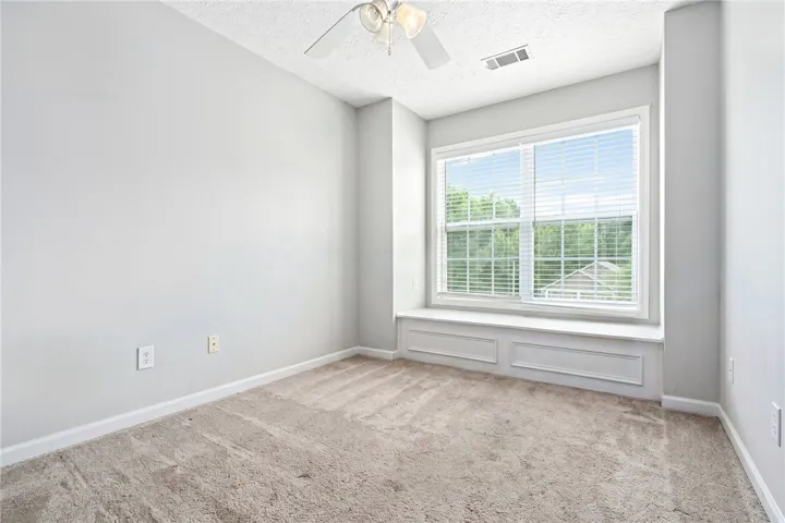 A well-lit bedroom features plush carpeting, a wide window, and a convenient window seat.