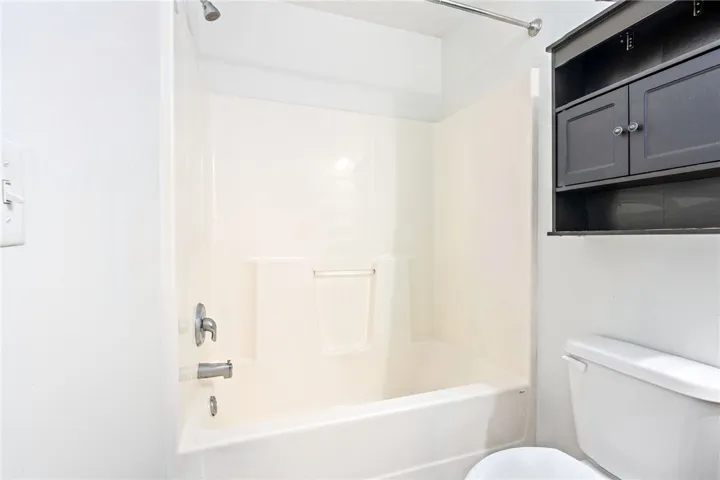 A pristine bathroom featuring a tub and shower combination, complemented by practical storage above the commode.