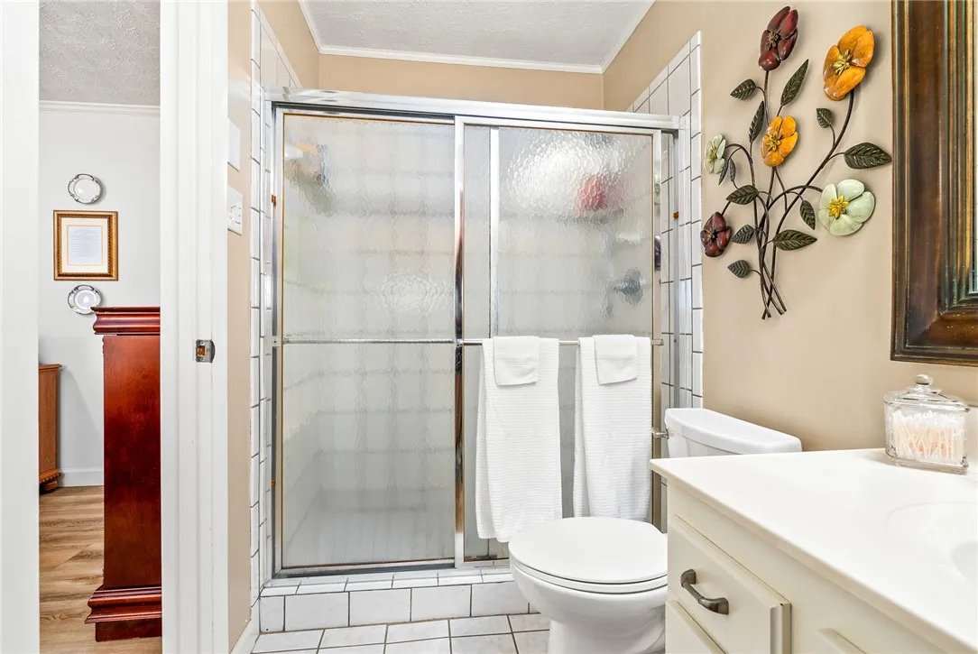 A compact full bathroom featuring a standing shower with sliding glass doors and a classic tile floor.