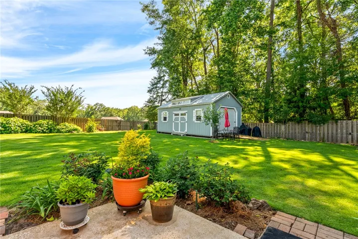 A vast, emerald lawn stretches towards a charming detached shed, bordered by mature trees and a private fence.