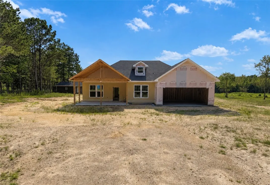 A new construction home awaits completion, nestled among trees with an attached garage.
