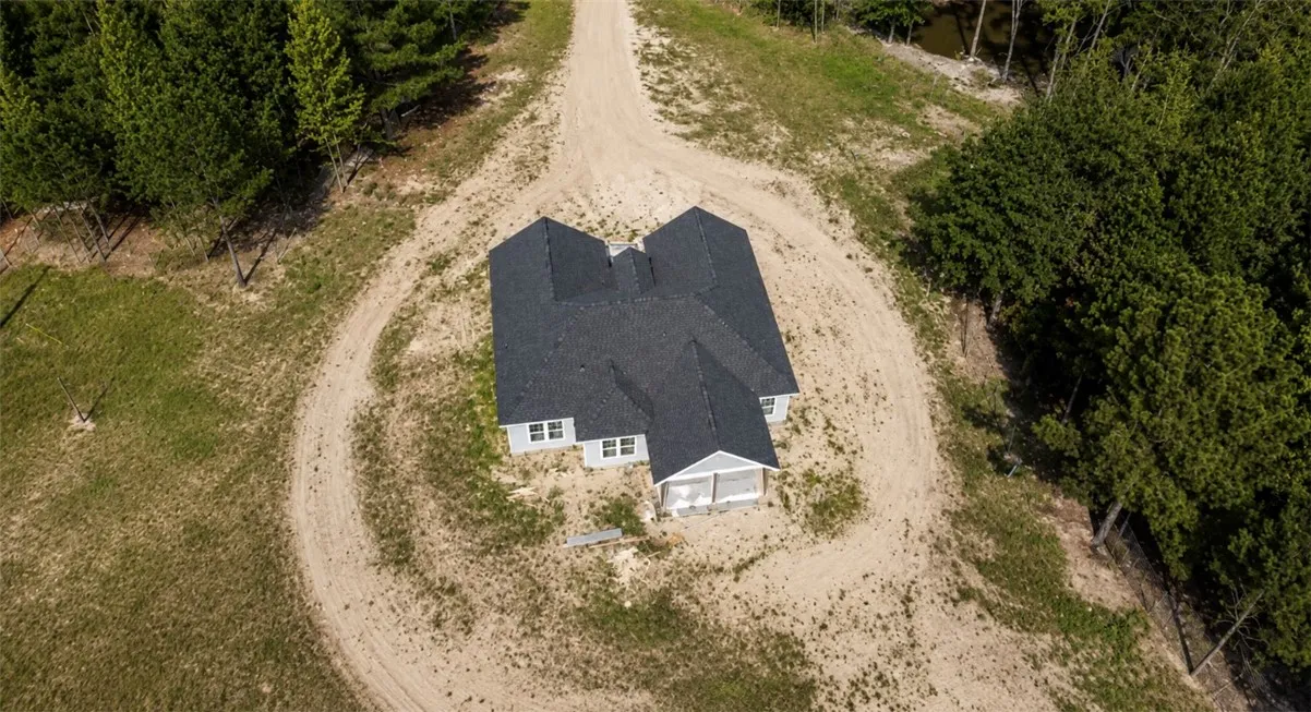 Perched on an expansive lot, this newly constructed residence features a winding driveway and wooded surroundings.