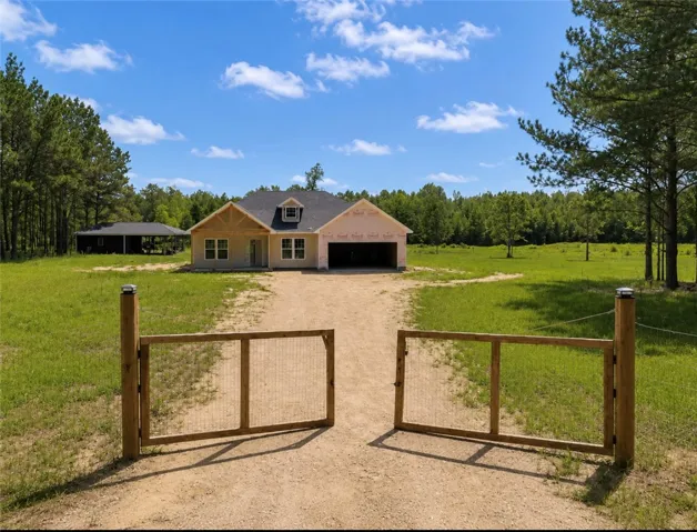 A new construction residence awaits behind a charming wooden gate, nestled amidst a verdant landscape.