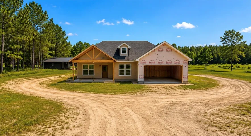A newly constructed residence is nestled among mature trees, with an attached garage and a long, winding driveway.