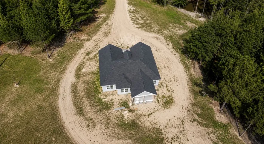Perched on an expansive lot, this newly constructed residence features a winding driveway and wooded surroundings.