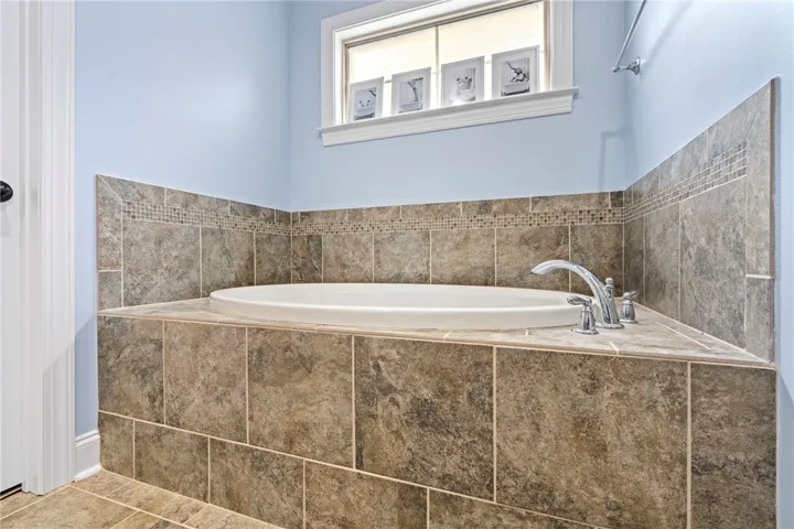 Unwind in the primary bath's generously sized soaking tub, encased in elegant tilework and set beneath a naturally illuminated window.