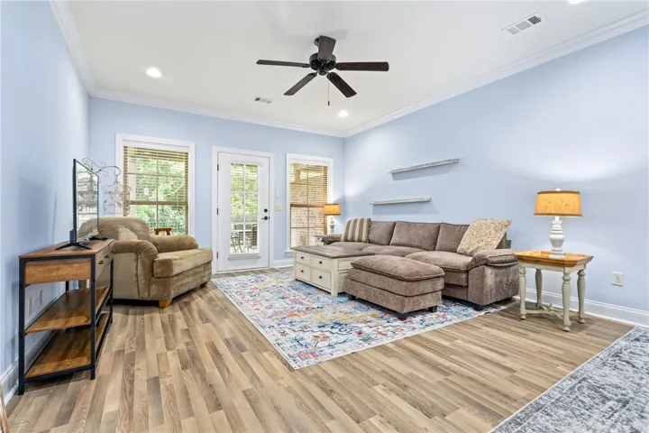 A comfortable living space boasts durable laminate flooring, a ceiling fan, and access to covered patio and fenced yard.