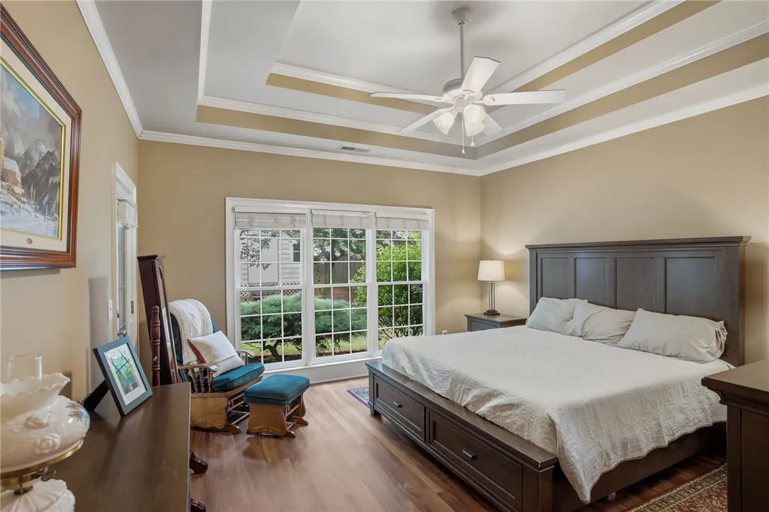 Hardwood floors and a stylish tray ceiling elevate this sunlit bedroom retreat.