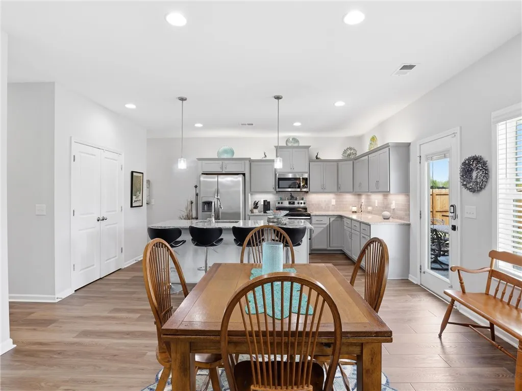 This naturally illuminated kitchen and dining area features an inviting island with a breakfast bar, complemented by modern appliances and durable wood flooring.