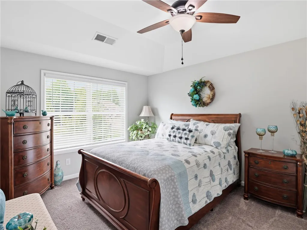 A naturally illuminated bedroom with a high ceiling, featuring a warm wooden bed frame and complementing furnishings.