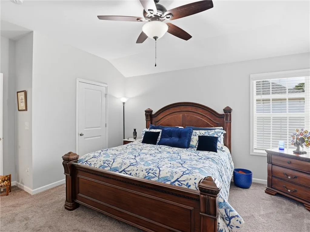 A vaulted ceiling crowns this restful primary bedroom, complete with soft carpeting and a bright window.