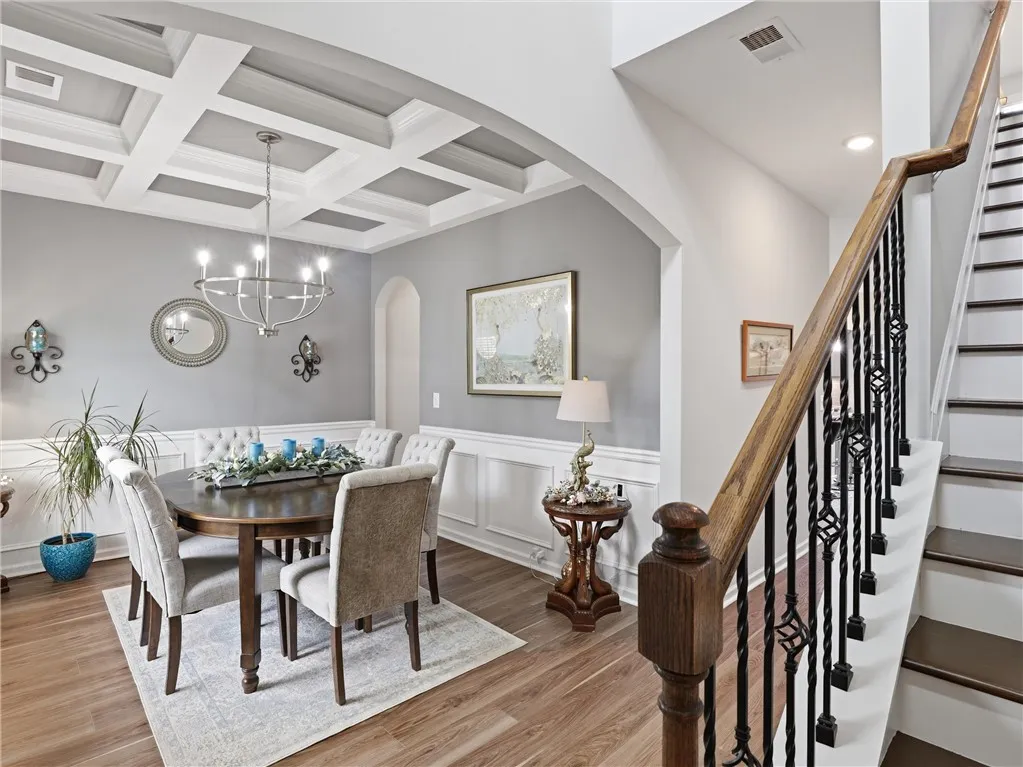 Elegant coffered ceilings crown this formal dining room, boasting rich wood flooring and classic wainscoting.