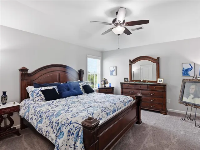 A well-lit bedroom featuring soft carpeting and a handsome wooden bed frame with matching dresser.