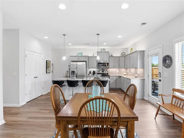 This naturally illuminated kitchen and dining area features an inviting island with a breakfast bar, complemented by modern appliances and durable wood flooring.