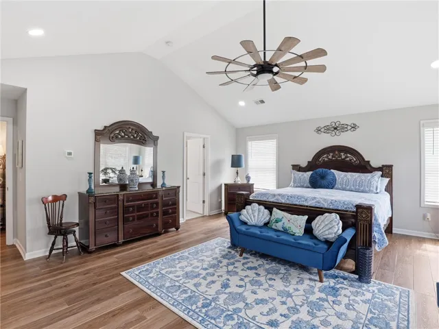 A vaulted ceiling and warm hardwood floors define this naturally illuminated primary bedroom.