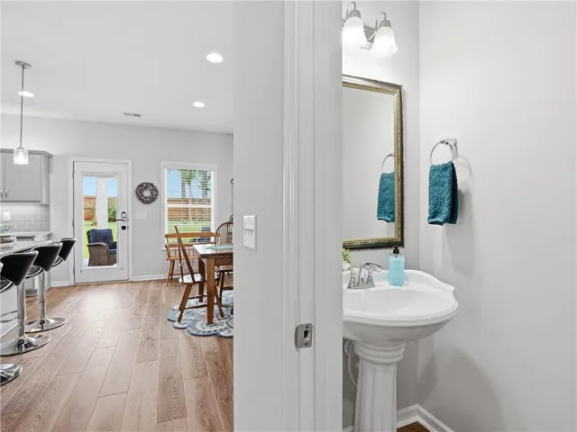 A well-appointed half bath features a pedestal sink and framed mirror, conveniently located near the dining area.