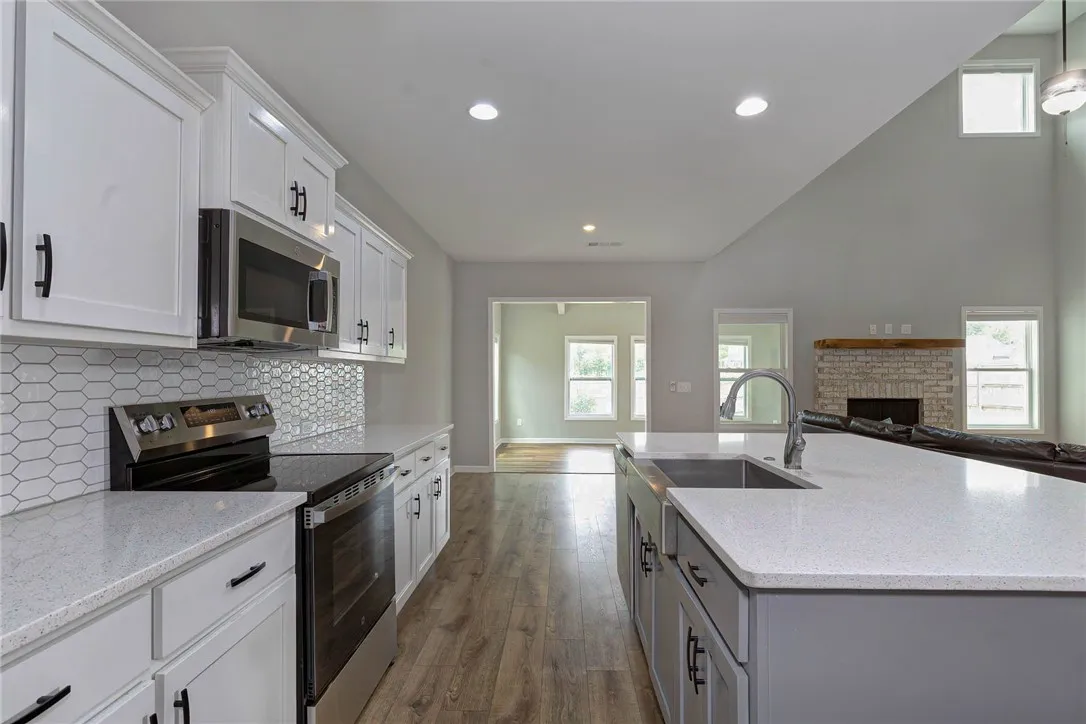 A contemporary kitchen boasts a spacious island and bright cabinetry, flowing into a living area with a brick fireplace.