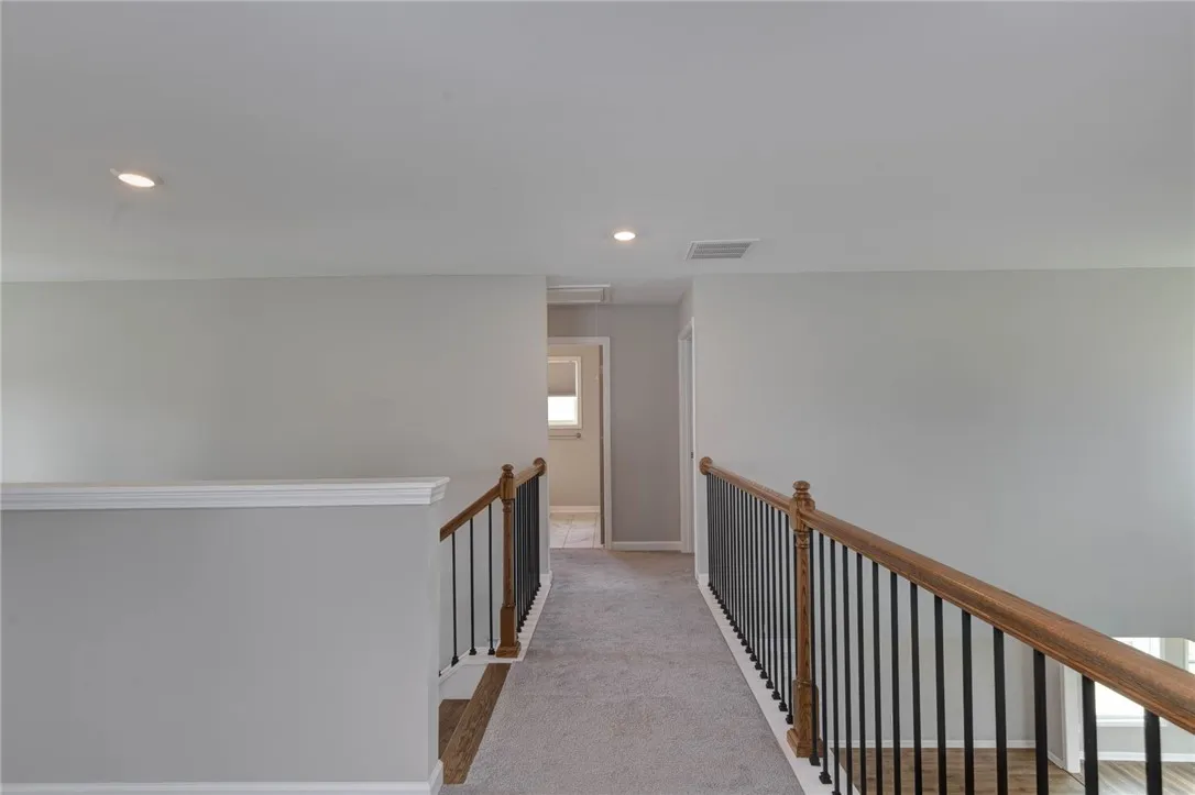 A well-lit second-story hallway with carpeted flooring and elegant wooden railings, offering a clean and inviting space.