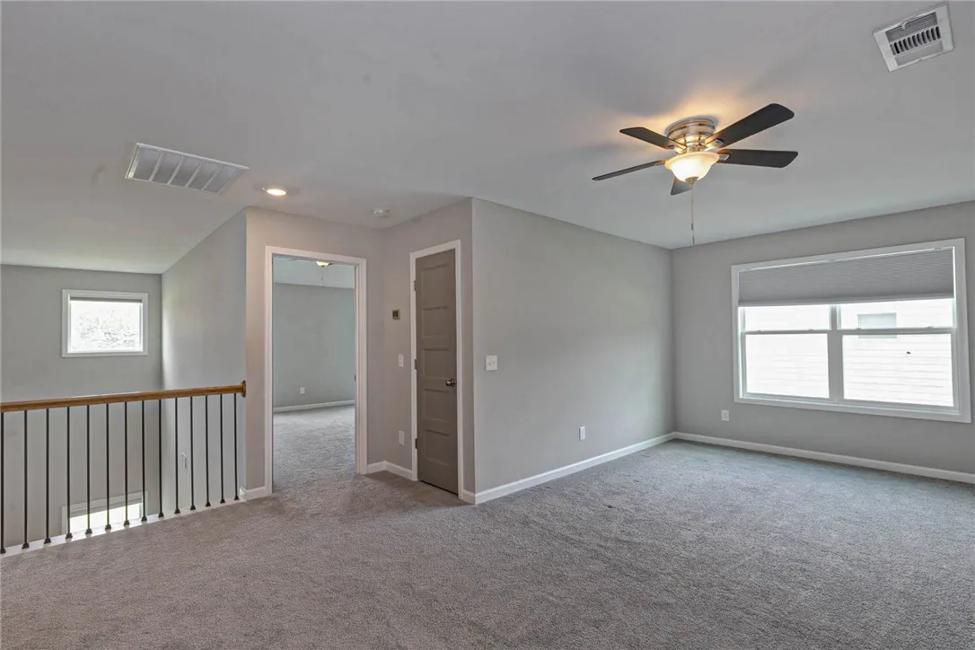 A well-lit upper level space with soft gray carpeting and a practical ceiling fan for comfort.