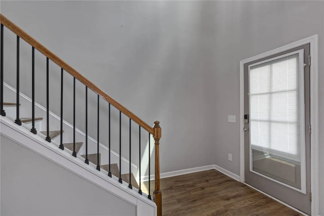 A graceful staircase with wood and iron accents leads to upper levels, beside a sun-lit entry with rich wood flooring.