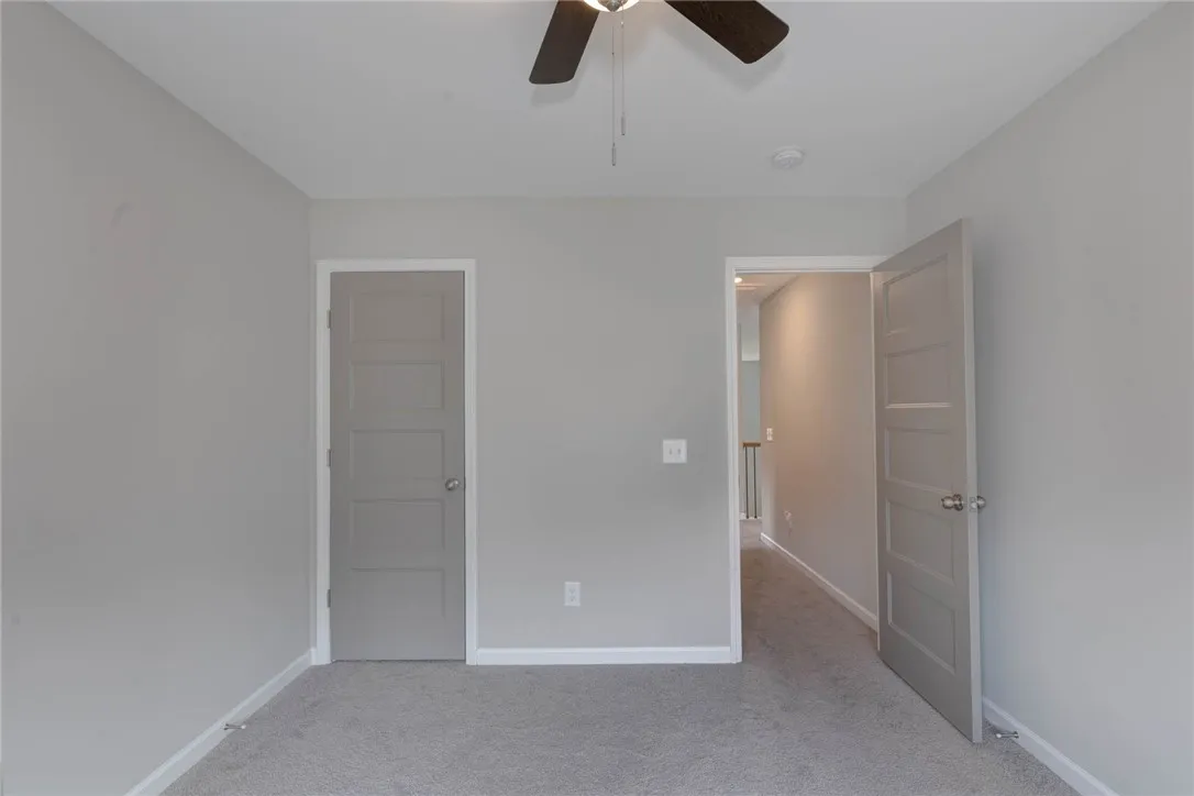 A well-lit bedroom features plush carpeting and a modern ceiling fan, offering a comfortable personal retreat.