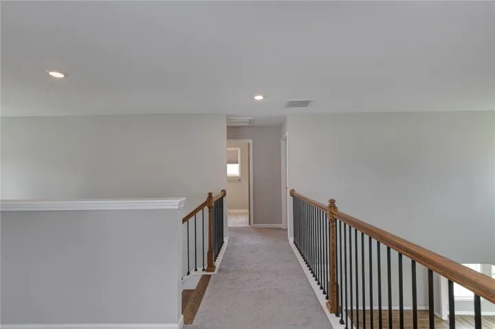 A well-lit second-story hallway with carpeted flooring and elegant wooden railings, offering a clean and inviting space.