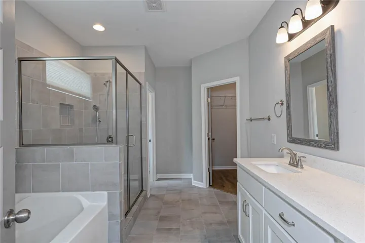 A well-appointed primary bathroom features a spacious glass-enclosed shower, separate soaking tub, and vanity with stone counters.